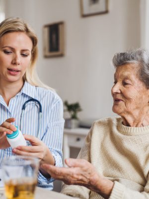 A young health visitor explaining a senior woman in wheelchair how to take medicine and pills.
